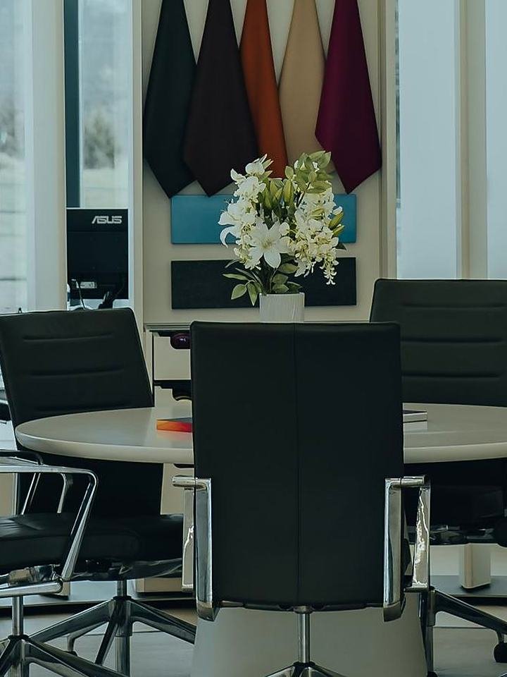 Mesa redonda de reunião num showroom, com amostras de tecidos e materiais na parede
