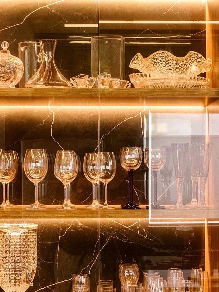 Vitrine iluminada de marcenaria com copos de cristal e loiça em prateleiras